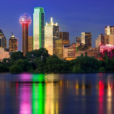 Illuminated by a blend of ambient and artificial light, sunset shimmers off the Dallas skyline as the city is reflected back in the flooded Trinity River. As the sun dips below the horizon, Bank of America Plaza (centered) glows iconic neon green, while lights on the iconic Reunion Tower (center left) flash red and blue, bringing the city to life as the night quickly approaches. (Photo/Stephen A. Masker).